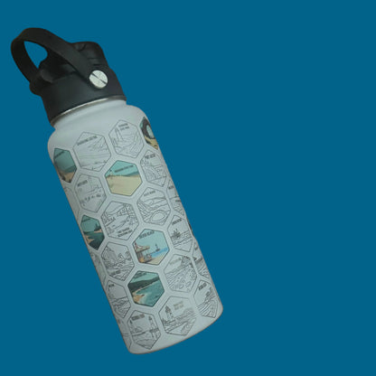 A reusable insulated water bottle with a black handle and a white body printed with a repeating hexagon pattern, resting on a dark brown wooden slat bench.